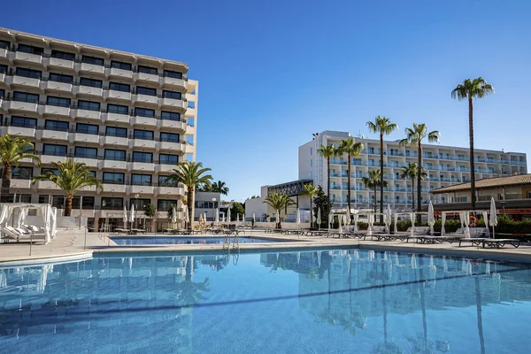 Ağaçlar ve lüks oteller manzaralı yüzme havuzu. Modern binaların, berrak mavi gökyüzüne karşı suyun içindeki yansıması. Yaz boyunca spa.