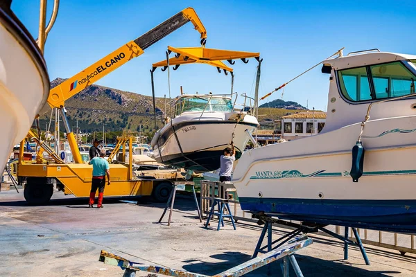 Mallorca, İspanya. 27 Nisan 2022. Sarı vinç limanda yelkenliyi kaldırıyor. İşçiler ağır makineler kullanarak denizden gemiler alıyorlar. Tersanedeki portatif asansör temiz gökyüzüne karşı..