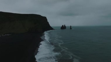 Reynisfjara Vik 'te büyük dalgaları olan İzlanda siyah kumsalı. Hava sineması 4K videosu. Güzel İzlanda doğa kıyısı yukarıdan.