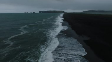 Reynisfjara Vik 'te büyük dalgaları olan İzlanda siyah kumsalı. Hava sineması 4K videosu. Güzel İzlanda doğa kıyısı yukarıdan.