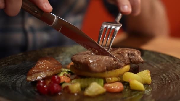 男の手はナイフを持ち フォークは鉄板の上で牛のステーキを焼きます 選択的焦点 — ストック動画