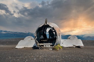 Siyah kum plajında terk edilmiş bir uçak enkazı. Gün batımında Solheimasandur 'da kırık bir askeri uçak. Bulutlu gökyüzüne karşı ünlü turistik cazibe manzarası.