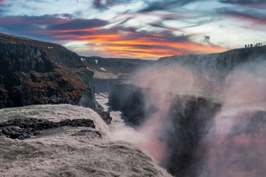 Altın Çember 'deki Gullfoss şelalesinin güzel manzarası. Bulutlu gökyüzüne düşen su manzarası. Gün batımında vadideki kaya oluşumları arasında çağlayanların resimli manzarası..