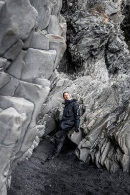 Güzel bazalt sütunlara karşı duran düşünceli bir turist. Deniz kıyısındaki kayalık oluşumu keşfederken gözlerini kaçıran bir adam. Ünlü Reynisfjara Sahili 'ndeki gri desenli taşlar..