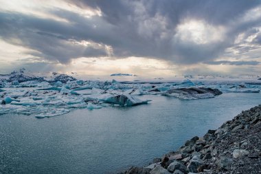 Dramatik gökyüzüne karşı Jokulsarlon Buzul Gölü 'nün Idyllic görüşü. Gölde yüzen güzel buzdağları. Gün batımında Vatnajokull 'da suda donmuş buzul oluşumlarının manzarası.