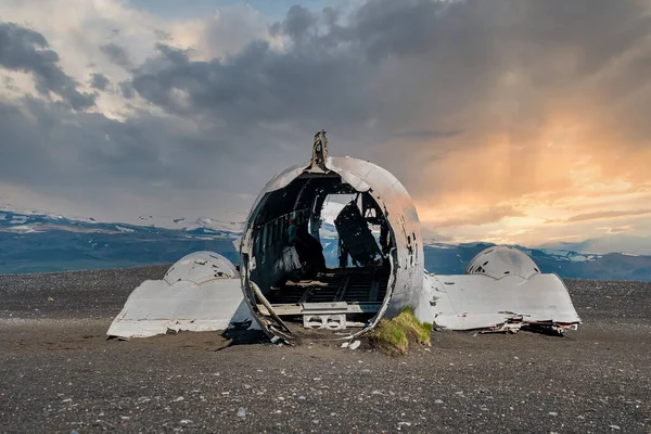 Siyah kum plajında terk edilmiş bir uçak enkazı. Gün batımında Solheimasandur 'da kırık bir askeri uçak. Bulutlu gökyüzüne karşı ünlü turistik cazibe manzarası.