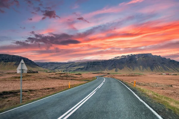 Dağ sırasına doğru giden boş otoyol. Volkanik arazide bulutlu gökyüzüne karşı azalan yolda yol işaretleri. Gün batımında yol kenarında sarı direkli cadde manzarası.
