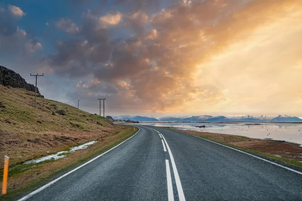 Deniz ve dağın ortasındaki karayolu azalıyor. Bulutlu gökyüzüne karşı boş sokaktaki yol işaretlerinin görüntüsü. Gün batımında volkanik vadideki güzel yol manzarası.
