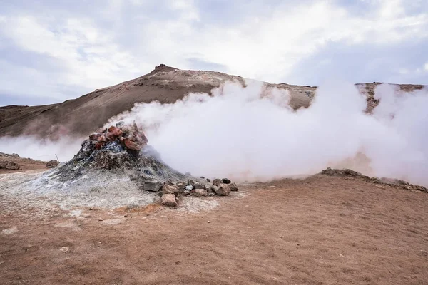 Steam emitting from fumarole in geothermal area of Hverir. Sulphur dioxide erupting from volcanic crater at Namafjall. Geyser in famous tourist attraction against cloudy sky.