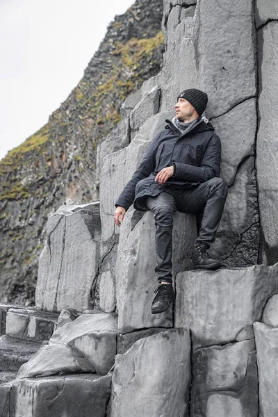 Turistler bazalt sütunlarda otururken gözlerini kaçırıyorlar. Deniz kıyısında kayalık oluşumda rahatlayan bir adam. Ünlü Reynisfjara Sahili 'ndeki gri desenli taşların manzarası..