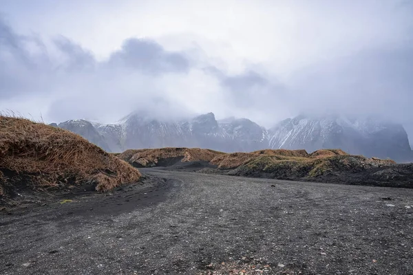 草の畑の中に黒い砂の道の眺め 曇りの空に対する山の風景です 霧の多い日の火山谷の美しい景色 — ストック写真