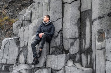 Erkek turist bazalt sütunlarda dinlenirken gözlerini kaçırıyor. Ünlü Reynisfjara Sahili 'ndeki gri desenli taşların manzarası. Gezgin, Rocky Cliff 'te boş vakitlerini geçiriyor..