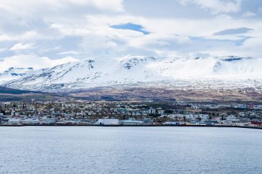 Deniz kıyısındaki şehir manzarasının manzarası. Bulutlu gökyüzüne karşı karla kaplı sıradağların güzel manzarası. Kış boyunca kentin ve doğal manzaranın ideal manzarası.