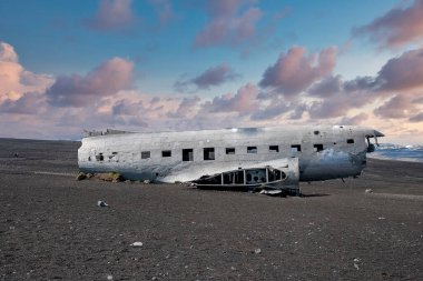 Siyah kum plajında terk edilmiş hasarlı uçak enkazı. Solheimasandur 'da kırık bir askeri uçak. Gün batımında bulutlu gökyüzüne karşı ünlü turistik cazibe.