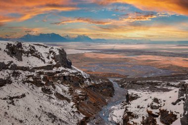 Karla kaplı dağların arasında akan güzel bir dere manzarası. Volkanik vadideki kaya oluşumlarının manzarası. Gün batımında gökyüzüne karşı uzanan Idyllic manzarası.