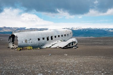 Kara Kumsal 'da terk edilmiş askeri uçak enkazı. Solheimasandur 'da bulutlu gökyüzüne karşı kırılmış bir uçak. Dağlara karşı turistik cazibe.