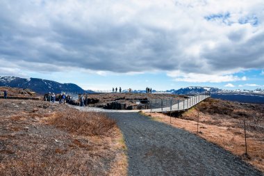 Dramatik manzarayı keşfeden turistler. Erkekler ve kadınlar köprüye doğru yürüyorlar. Thingvellir Milli Parkı 'nda bulutlu gökyüzüne karşı güzel bir dağ.