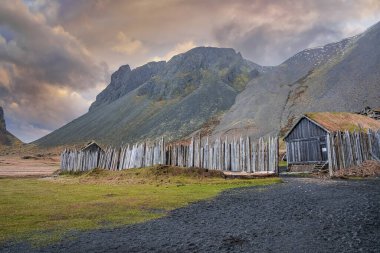 Ahşap çitlerle çevrili geleneksel evler. Vestrahorn Dağı 'nın altındaki ortaçağ Viking köyü. Stokksnes 'deki güzel tarihi yerleşim günbatımında dramatik gökyüzüne karşı.