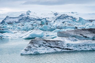 Jokulsarlon buzulu gölünde yüzen buzdağlarının manzarası. Bulutlu gökyüzüne karşı gölde güzel buzul oluşumları. Vatnajokull 'da sıradışı hava koşullarında ideal manzara.