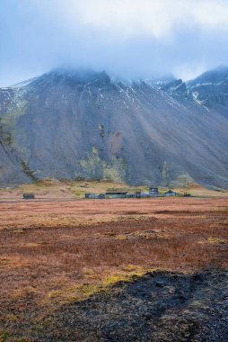Stoksnes yakınlarındaki terk edilmiş Viking köyünün uzak görüşü. Görkemli Vestrahorn dağının altında bulutlarla kaplı geleneksel evler. Güzel ortaçağ turistik cazibesi volkanik manzaranın ortasında.
