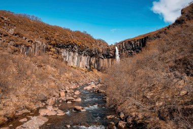 Bazalt sütunların ortasındaki Svartifoss şelalesinin manzarası. Ulusal parktaki uçurumlardan akan akıntı mavi gökyüzüne karşı. Ünlü turistik mekanın manzarası.