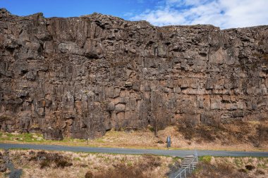 Parmaklıklı yol boş yola çıkıyor. Thingvellir Ulusal Parkı 'ndaki görkemli kaya oluşumlarının manzarası. Gökyüzüne karşı volkanik manzaradaki güzel uçurum manzarası.