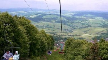Kayak merkezinde teleferik. Yazın yeşil çimen ve kar olmadan çekiliyor. Güneşli yaz günlerinde kulübelerin çalıştığı yüksek uzun bir teleferik hattı. Yaz aylarında dağda seyahat ve turizm kavramı.