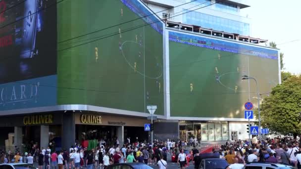 大画面でサッカーを見ている多機能複合ガリバー ビジネスやエンターテイメントスポットと混雑した街の通りや道路交通 — ストック動画