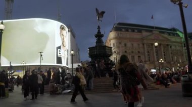 Londra 'daki Piccadilly Sirki' nde gece hayatı. İnsanlar karşıdan karşıya geçiyor ve ikonik kırmızı çift katlı otobüsler reklam pankartlarıyla Piccadilly Sirki 'nden geçiyor.. 
