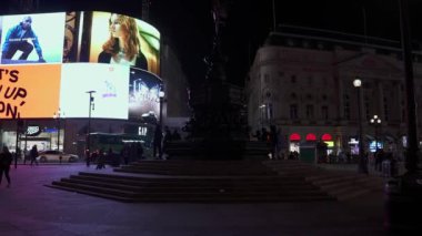 Londra 'daki Piccadilly Sirki' nde gece hayatı. İnsanlar karşıdan karşıya geçiyor ve ikonik kırmızı çift katlı otobüsler reklam pankartlarıyla Piccadilly Sirki 'nden geçiyor.. 
