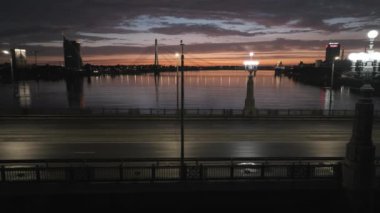 Riga 'da gün batımında gece köprünün yanında. Letonya 'nın Riga şehrinin üzerinde uçuyor. Güzel destansı gün batımı.