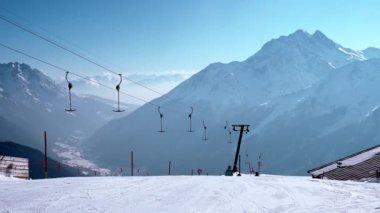 Avusturya Alpleri 'ndeki karlı arazide kayak asansörü hareket ediyor. Başkanlık, açık mavi gökyüzüne karşı. Turistler Alplerdeki kayak merkezinde kışın keyfini çıkarıyorlar.