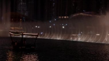 Dubai 'de gece vakti Burj Halife gökdeleninin önünde fıskiye gösterisi. Burj Halife binasının önündeki çeşmeler. 4k video.