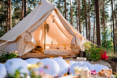 Boho tarzında güzel beyaz bir dekor. Doğada piknik, masa, halılar, çadır, parkta yastıklar. Doğa konseptinde tatiller.