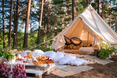 Boho tarzında güzel beyaz bir dekor. Doğada piknik, masa, halılar, çadır, parkta yastıklar. Doğa konseptinde tatiller.