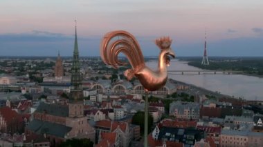 Riga 'da gün batımında Kubbe Katedrali' nin tepesindeki altın horoz. Ortasında altın bir horoz olan güzel bir şehir manzarası. Gün batımı zamanı.