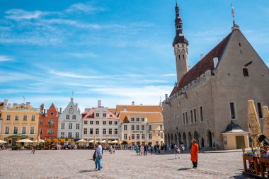 Tourists walking by cathedral while exploring market at city square. People wandering on cobblestone street in old historic town against sky. View of residential buildings during sunny day.