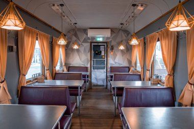 Tables and seats arranged in illuminated train coach restaurant. Interior of stationary railroad vehicle restaurant of Peatus. Famous tourist attraction in historic old town Tallinn