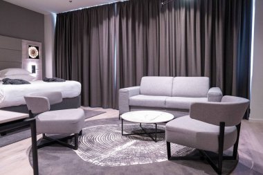 Perdelere karşı rahat kanepesi olan orta masa. Temiz yatağa dizilmiş havlu ve yastıklar. Lüks tatil beldesindeki rahat, modern yatak odasının içi..