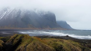 Siyah kumsalın kıyısındaki güzel çimen manzarası. Stoksnes Pelerini ve Vestrahorn Dağı 'nın İzlanda' daki sisle kaplı manzarası. İzlanda 'nın ünlü turistik mekanının ideal manzarası.