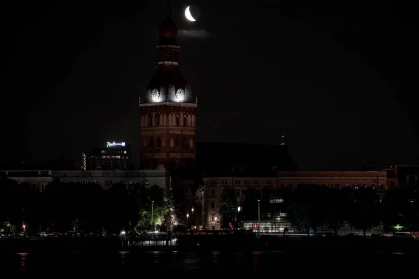 Beautiful quarter moon over Riga old town behind Domes cathedral clock. Night sky with amazing moon.