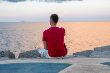 Gezinti güvertesinde dinlenen bir adamın arka görüntüsü. Erkek turist deniz kenarında otururken sahile bakıyor. Tatilde boş zamanlarının tadını çıkarırken gündelik giysiler giyiyor..