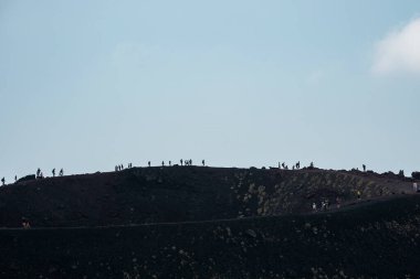 Etna Dağı 'ndaki volkanik kraterde yürüyüş yapan insanlar. Arka planda dumanla kaplı gökyüzü ile dramatik manzara. Turistler ünlü eğlence için maceralı bir tatil yapıyorlar..