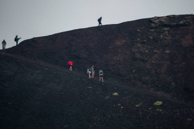 Erkek ve kadın turistler Etna Dağı 'ndaki kraterde yürüyüş yapıyorlar. Arka planda dumanla kaplanmış volkanik manzaranın görüntüsü. Erkekler ve kadınlar popüler eğlence için maceralı bir tatil yapıyorlar..