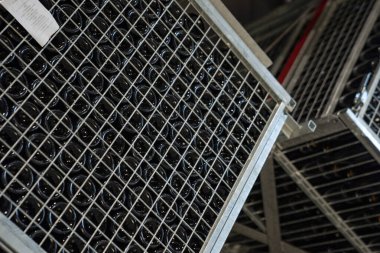 Şaraphanedeki metal kaplarda dizilmiş cam şişeler. Depoda mayalanmış taze üzüm şarabı koleksiyonu. Şarap üretim prosedürü depoda.
