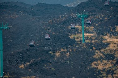 Volkanik arazide hareket eden teleferiklerin yüksek açılı görüntüsü. Meşhur Etna Dağı 'nda ulaşım modu. Popüler turizm merkezinde külle patlamış kraterin manzarası.