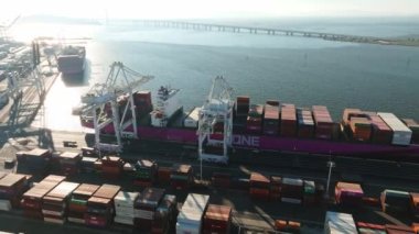 Gün batımında tersanede çalışan vinç köprüsü olan konteyner kargo gemisinin lojistik ve taşımacılığı. Lojistik ihracat ve ulaşım sektörü 4k hava videosu.