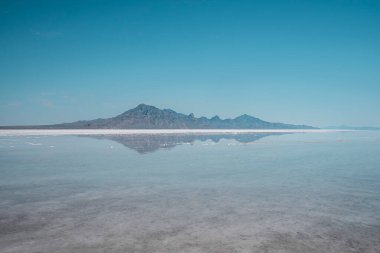 Scenic view of Bonneville salt flat and mountains. Beautiful peak reflecting in tranquil water with clear sky in background. Picturesque scenery of famous tourist attraction during summer. clipart