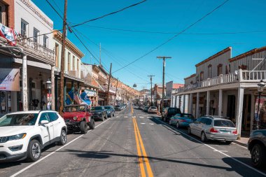 Virginia, ABD. Virginia 'nın tarihi kovboy kasabasındaki eski dükkanların arasına park etmiş arabalar. Kasabadaki eski binalar ve elektrik sütunlarının arkasında mavi gökyüzü var. Yazın boş yol.
