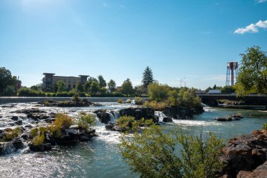 Beautiful snake river at Idaho falls flowing by museum. Rapid water amidst rocks and plants with blue sky in background. Natural scenery of famous tourist attraction in city during sunny day. clipart